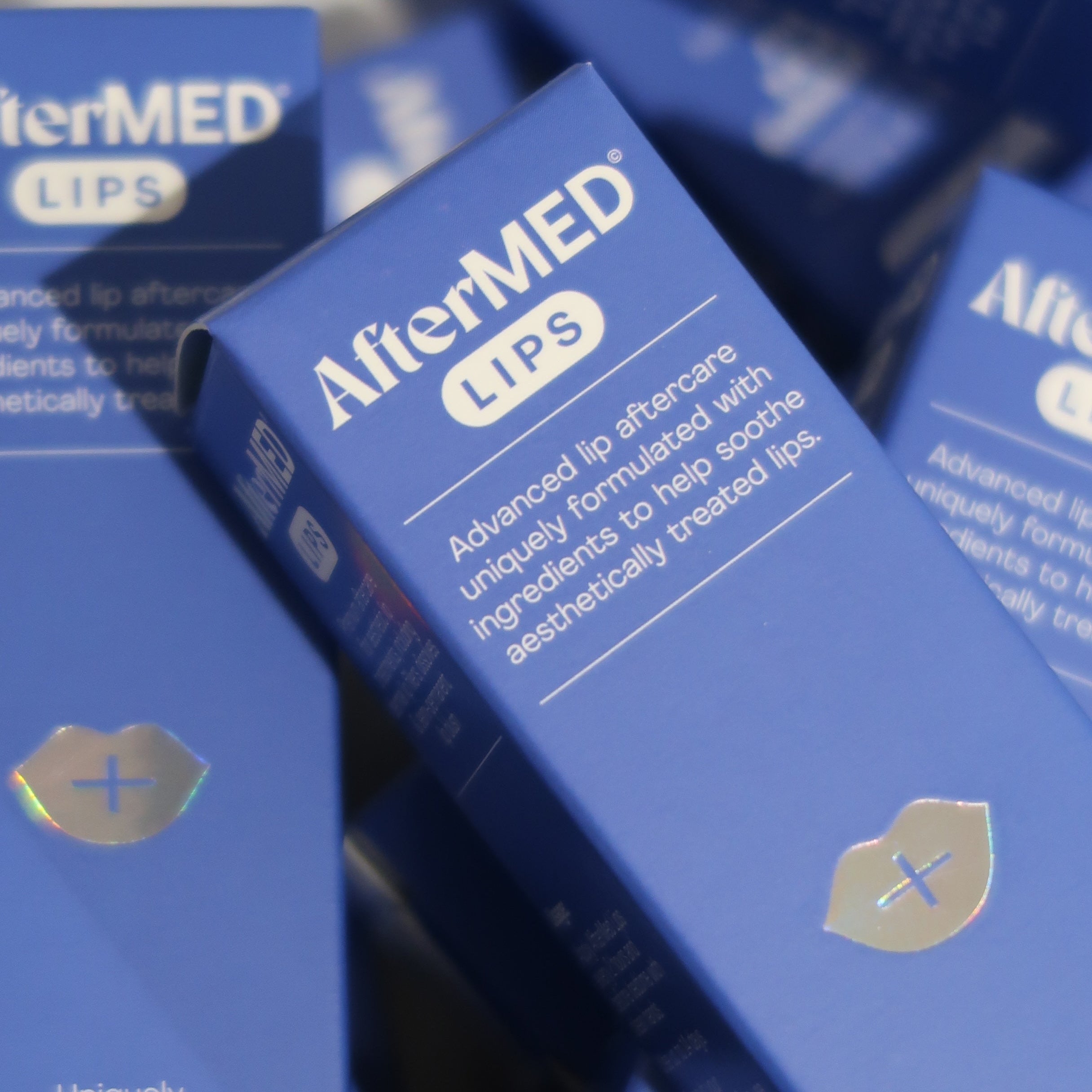 Multiple boxes of AfterMED Lips product on a blue background
