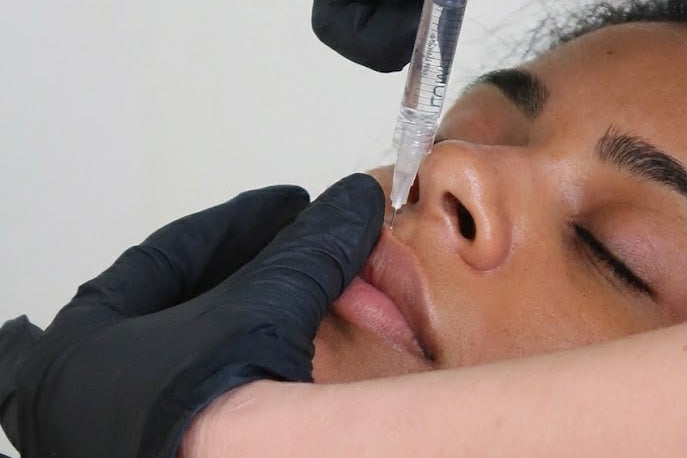 Person receiving a facial injection with gloved hands holding a syringe.